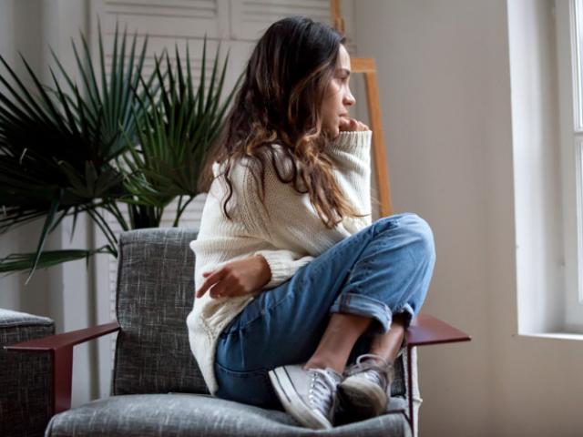 Chica sentada mirando por la ventana que quiere saber cómo calmar la ansiedad.